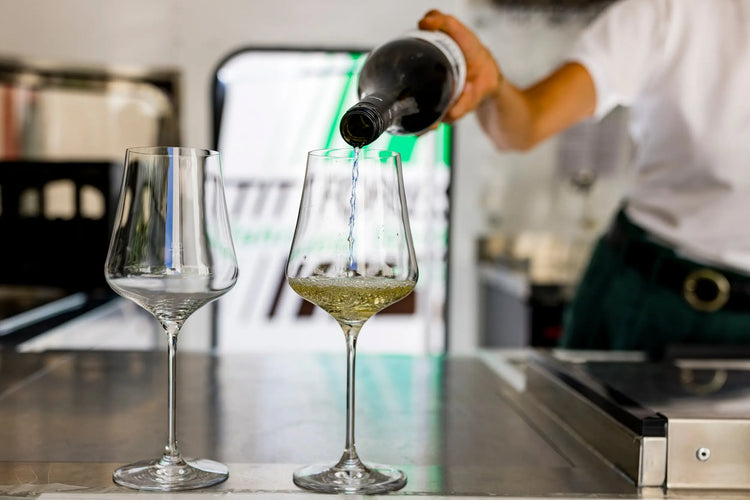 Weißwein wird in ein Weinglas auf Tresen gegossen, zwei Gläser im Fokus, Sommercocktail Szene